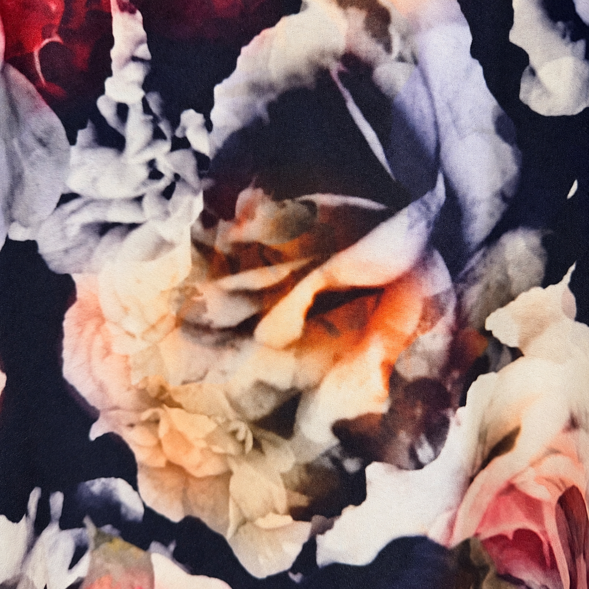 A close-up of a floral fabric print featuring large watercolor-style roses in cream, blush pink, peach, and dark navy/black tones.