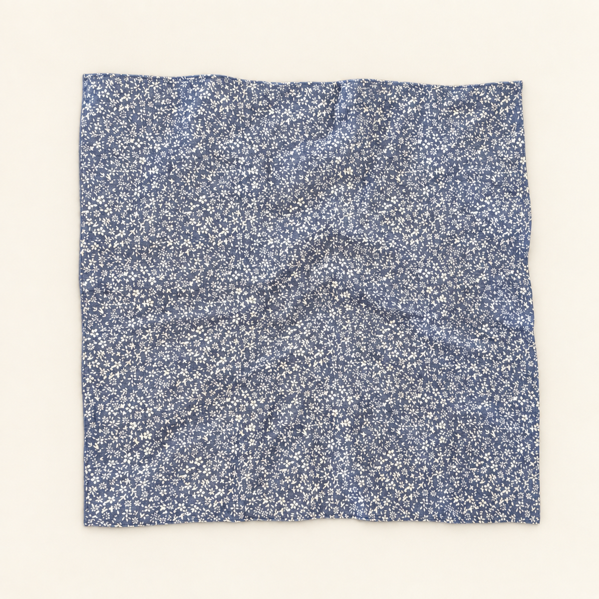 A square piece of blue fabric with a dense white floral or ditsy print, laid flat against a solid off-white background.