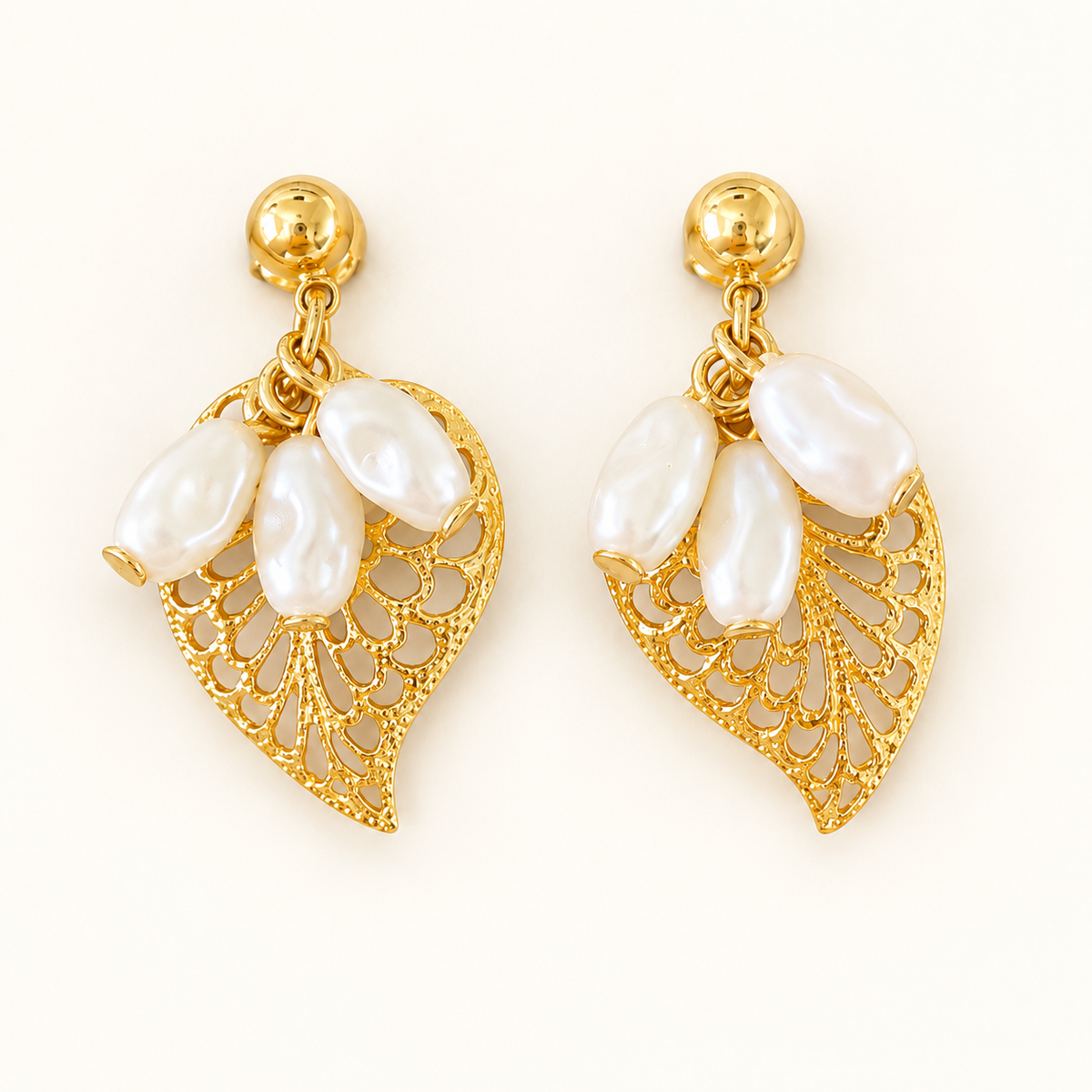 A pair of gold leaf-shaped dangle earrings with white baroque pearls, shown on a clean off-white background.
