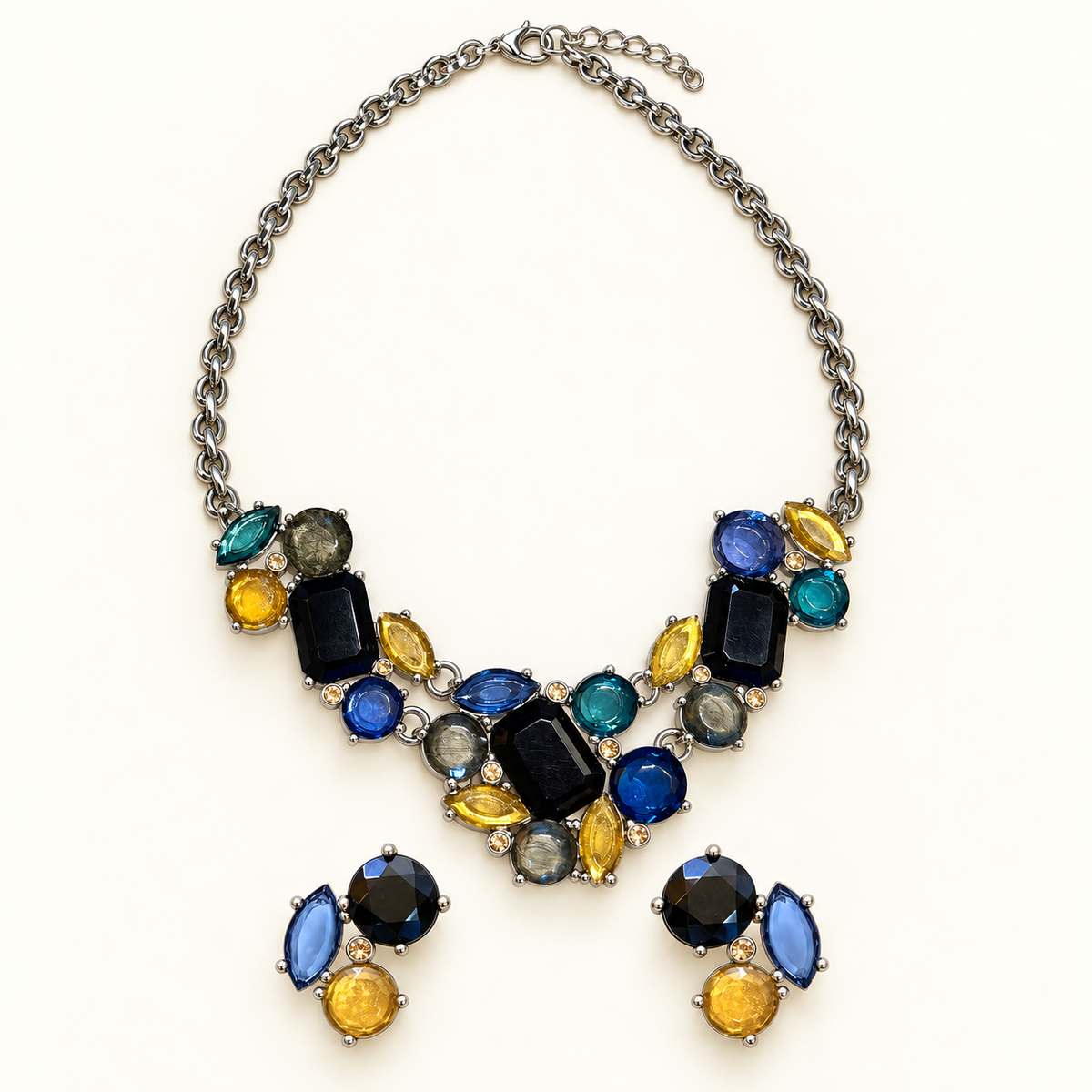 A silver-tone statement necklace with a matching pair of drop earrings, featuring a variety of colored gemstones including blue, yellow, black, green, and gray on a plain white background.