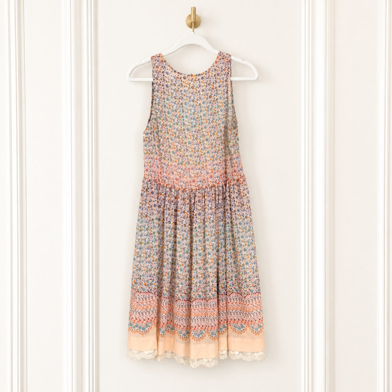 A sleeveless tiered dress with a multicolor floral and geometric pattern, hanging on a white hanger against a white paneled door.