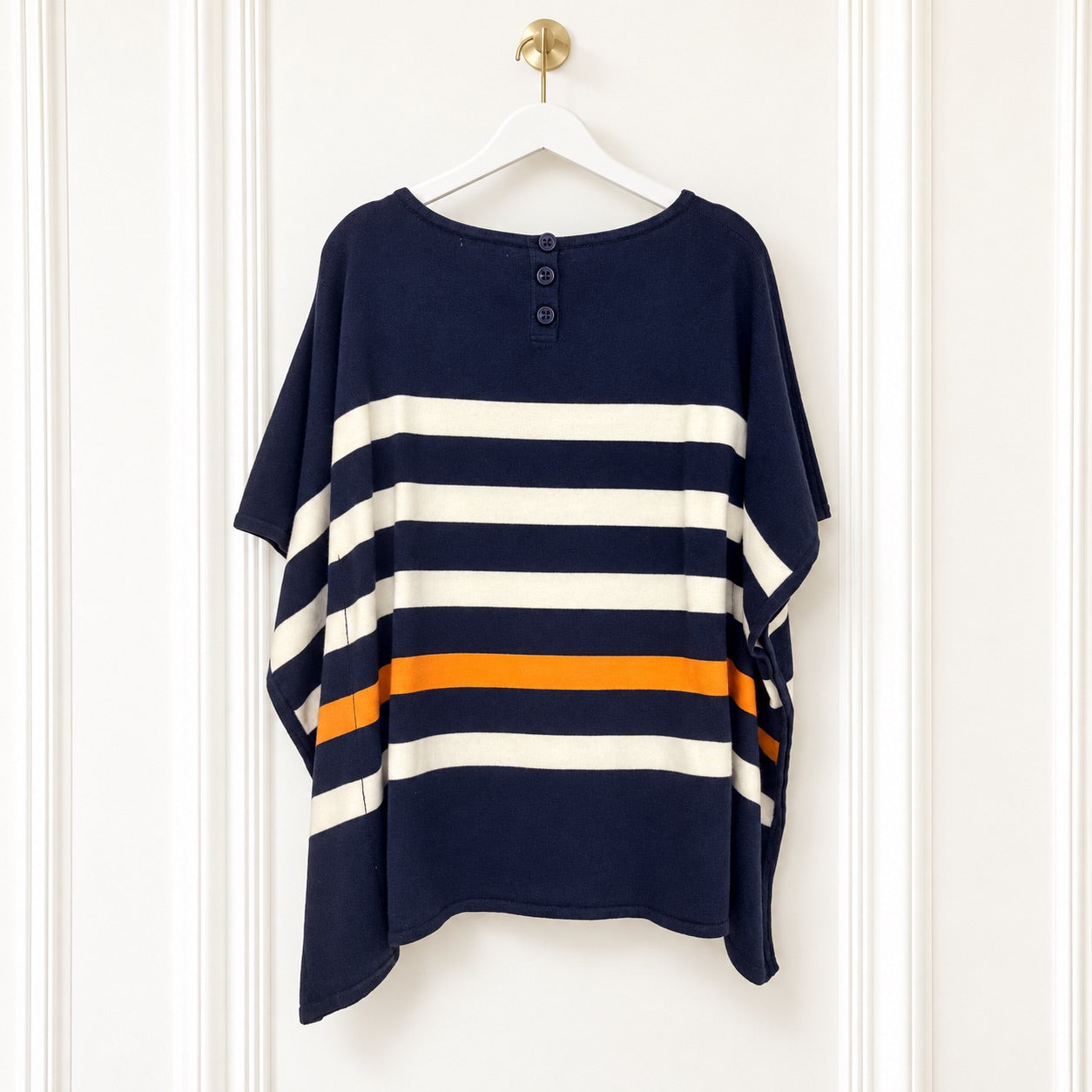 A navy blue short-sleeve tunic top with horizontal cream and orange stripes, hanging on a white hanger against a white paneled door.