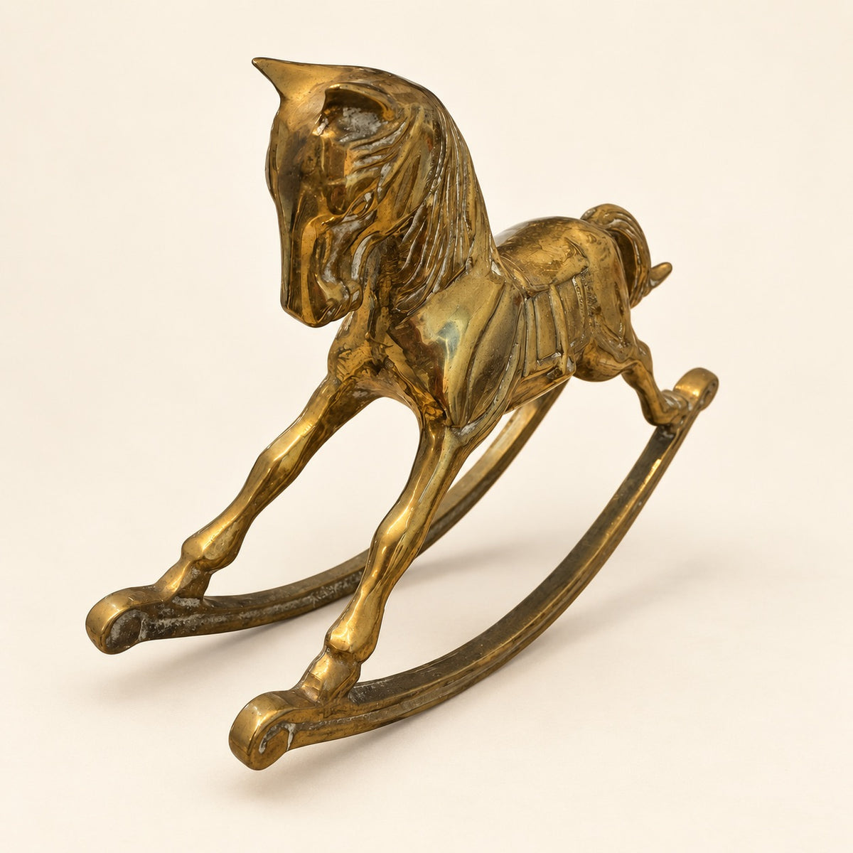 A small metallic golden rocking horse figurine on a plain light beige background.