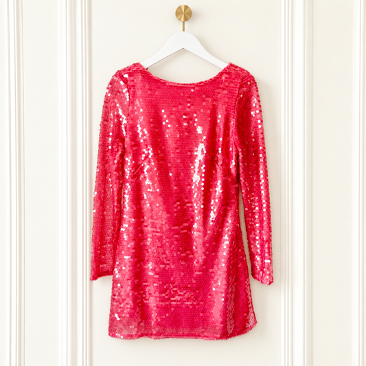 A bright pink sequined long-sleeve top hanging on a white hanger against a white paneled door.