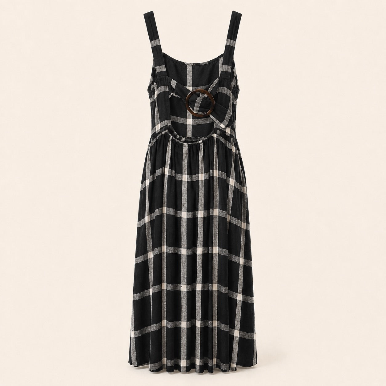 A sleeveless black and white plaid midi dress with a round brown wooden ring detail at the center bust, displayed on a neutral cream background.