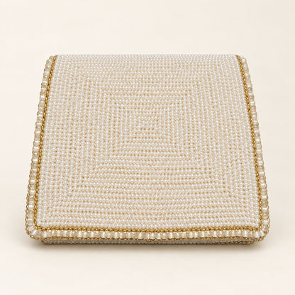 A square, flat-lay view of a cream and gold beaded box or clutch with a textured pearl-like pattern and a gold-trimmed border, set against a solid cream background.