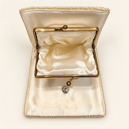 An open vintage-style clutch case with a cream satin interior, gold-tone metal frame, and a beaded border trim, photographed on a plain light background.