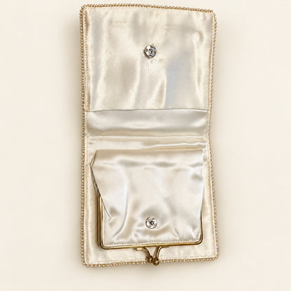 An open satin wallet or clutch in a warm ivory or cream tone, featuring a decorative beaded border, a top snap closure, and a smaller front pocket with a bottom snap closure.