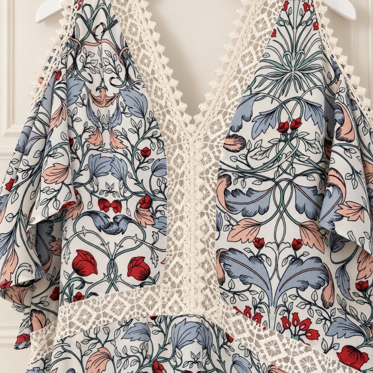A close-up of a garment featuring a William Morris-style floral and animal print with blue-gray leaves, pink and red floral accents, and a cream lace overlay.