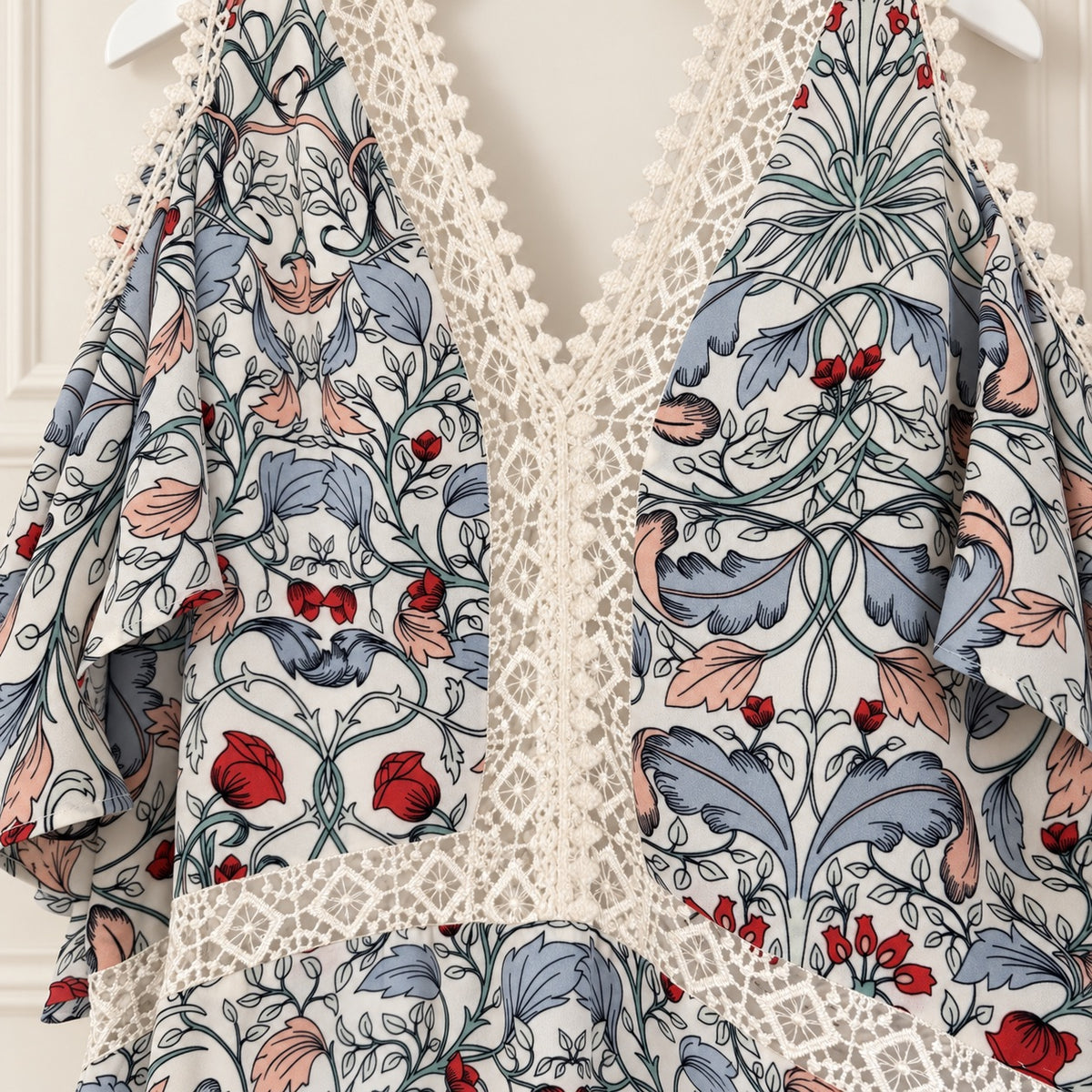 A close-up of a garment featuring a William Morris-style floral and animal print with blue-gray leaves, pink and red floral accents, and a cream lace overlay.