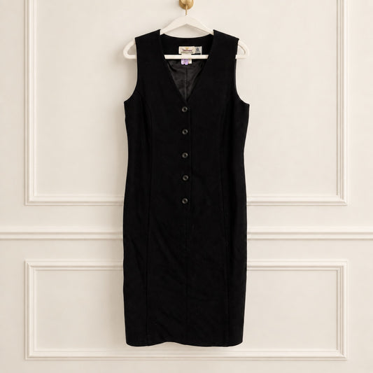A sleeveless black dress with a V-neck and a vertical row of buttons down the front, hanging on a white hanger against a white paneled wall.