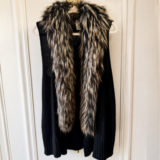 A black knit sweater vest with a thick, shaggy faux fur collar in black, brown, and white, hanging on a white hanger against a white paneled door.