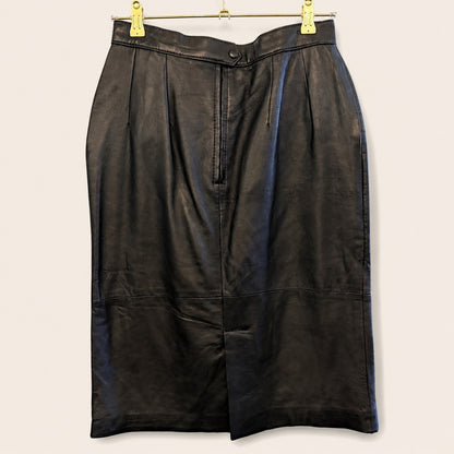 A black leather pencil skirt with pleated detailing, hanging from a gold metal hanger with gold clips against a light beige background.