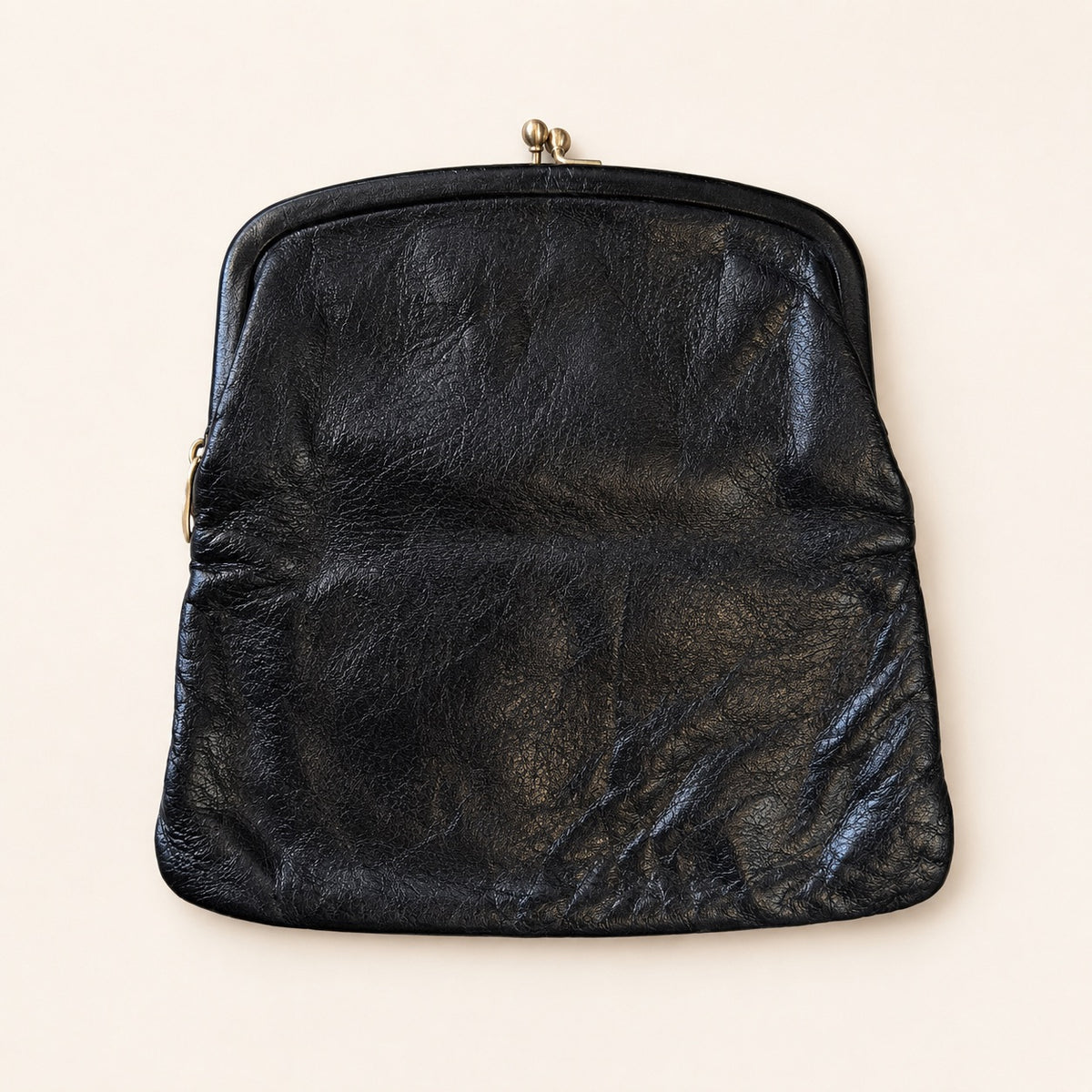 A vintage black leather kiss-lock clutch bag with a gold-tone metal clasp, displayed flat against a light beige background.