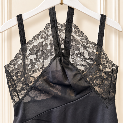 Black satin slip dress with floral lace cups and thin shoulder straps, hanging on a white hanger against a cream paneled door.