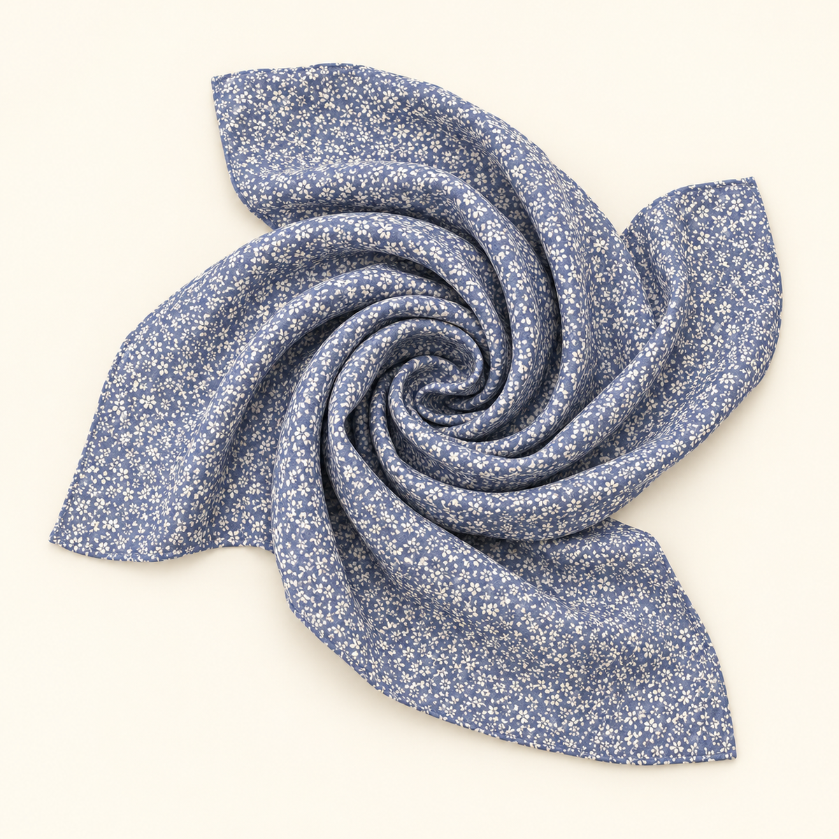 A square scarf with a dense white floral print on a dusty blue background, styled in a spiral drape on a solid cream-colored background.