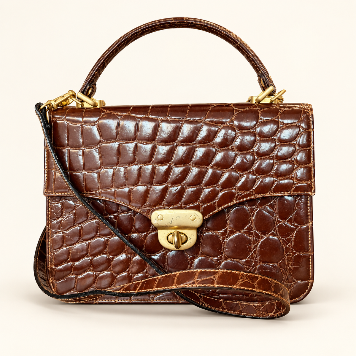 A brown crocodile-embossed leather handbag with a top handle, a detachable shoulder strap, and gold-tone hardware, photographed against a plain light background.