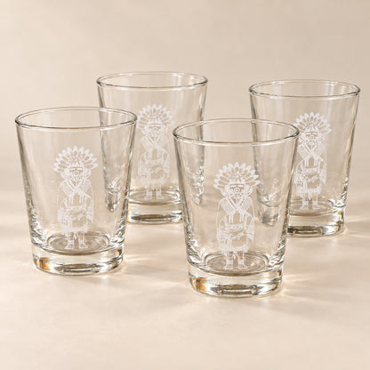 Four clear glass tumblers with white etched Native American-style figures, arranged on a warm beige surface against a matching beige background.