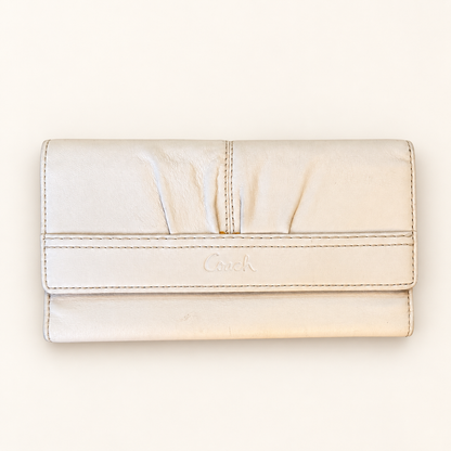A Coach leather clutch wallet in a light cream or off-white color, featuring a stitched horizontal band with the embossed Coach logo and a vertical center seam.