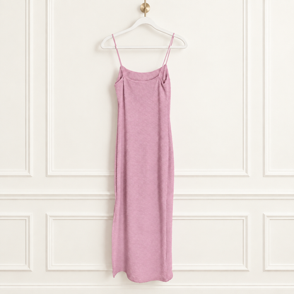 A dusty pink knit slip dress with thin spaghetti straps, hanging from a white plastic hanger against a white paneled wall.