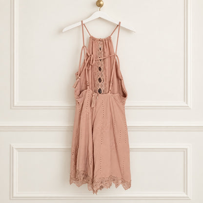 A dusty rose eyelet lace halter dress with tie-front details and a scalloped lace hem, hanging on a white hanger against a white paneled wall.