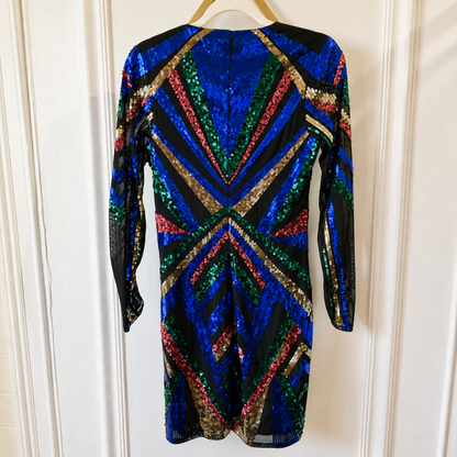 A long-sleeve sequined dress hanging on a wooden hanger against a white paneled door. The dress features a vibrant geometric pattern with blue, green, red, and gold sequins on a black base.