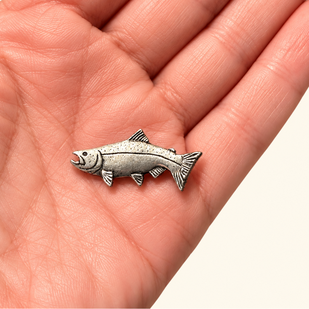 A small silver fish-shaped charm or pendant resting on an open human hand, shown against a plain light background.