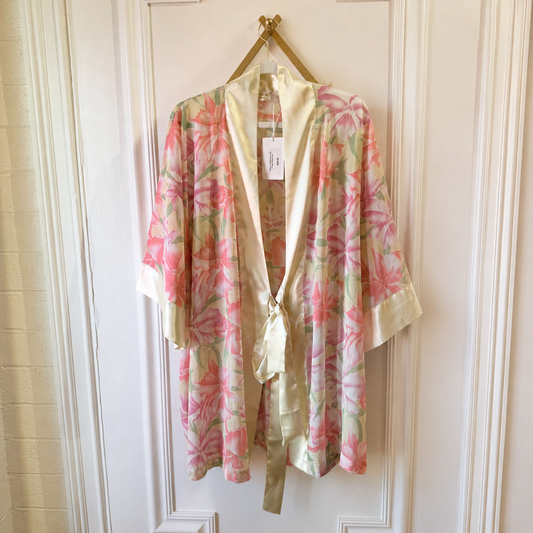 A lightweight floral robe with pink and green floral print and cream satin trim, hanging on a gold hanger against a white paneled door.