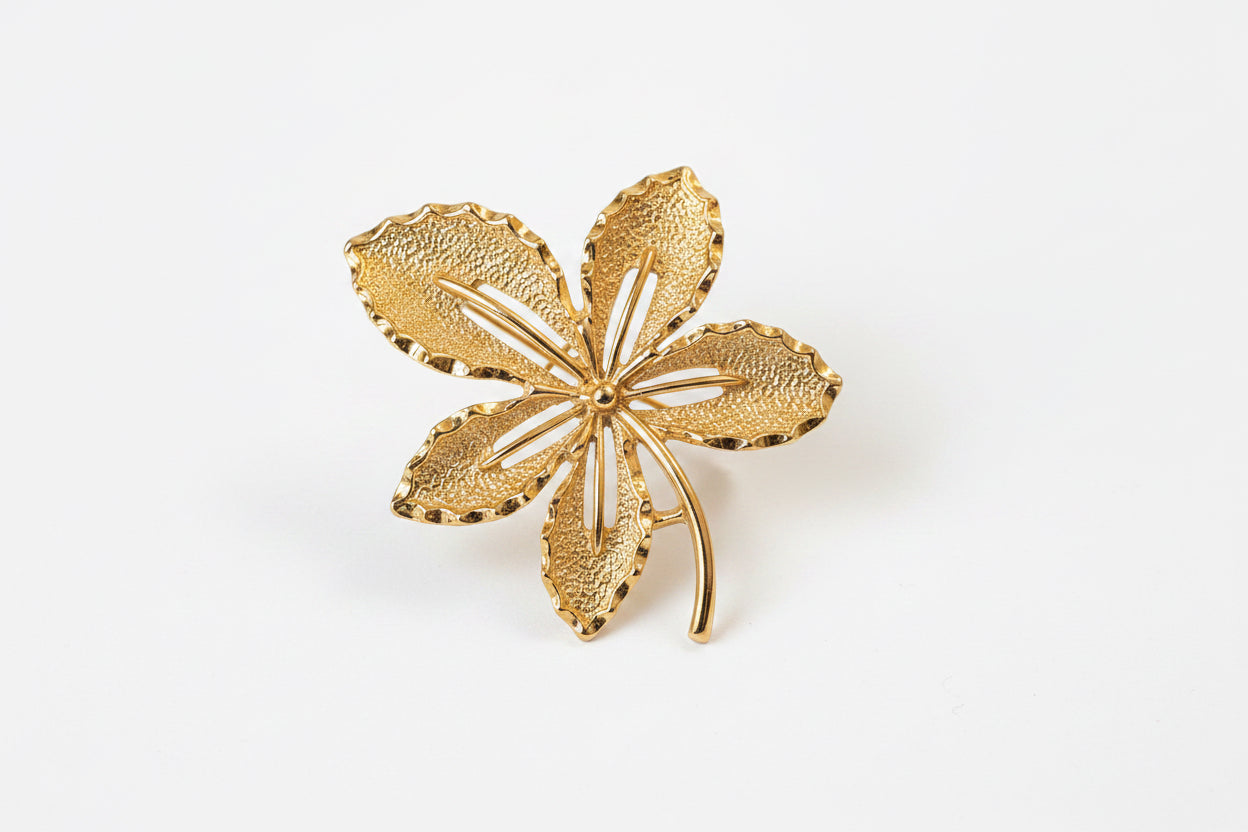 A textured gold-tone flower-shaped brooch with five petals and open center details, displayed on a dark green velvet background.