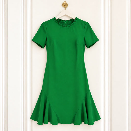 A bright green short-sleeve dress with a ruffled neckline and a flared ruffle hem, hanging on a white hanger against a white paneled door.
