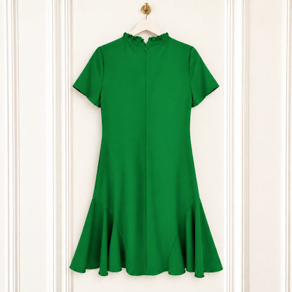 A bright green short-sleeve dress with a high ruffled mock neck and a flared ruffle hem, hanging on a white hanger against a white paneled door.