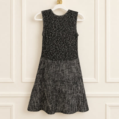 A sleeveless black and gray textured dress hanging on a white hanger against a cream paneled wall.