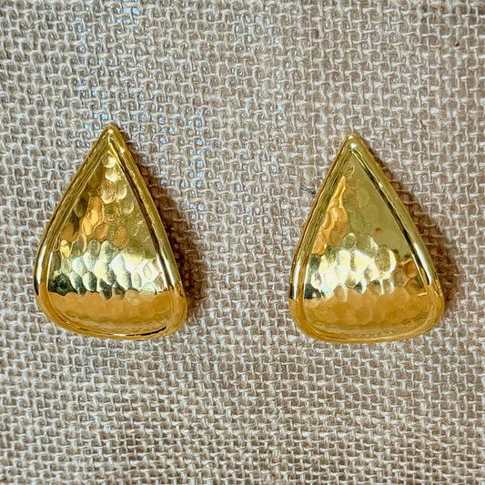 A pair of gold teardrop-shaped earrings with a hammered texture, displayed on a beige woven fabric background.