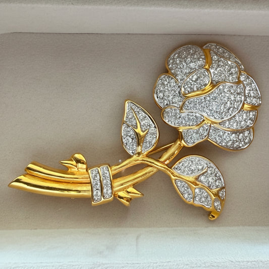 A gold and diamond rose brooch displayed inside a light beige jewelry box.