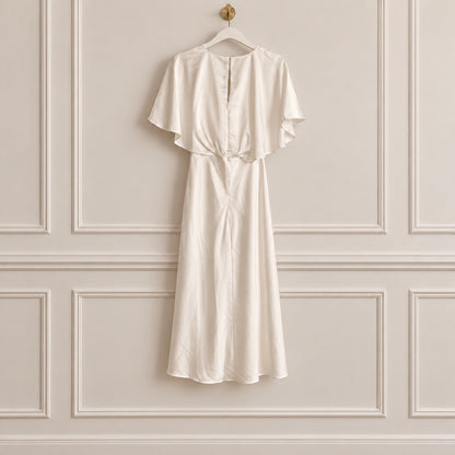 An ivory or cream-colored midi dress with short flutter sleeves and a gathered waist, hanging on a white hanger against a beige paneled wall.