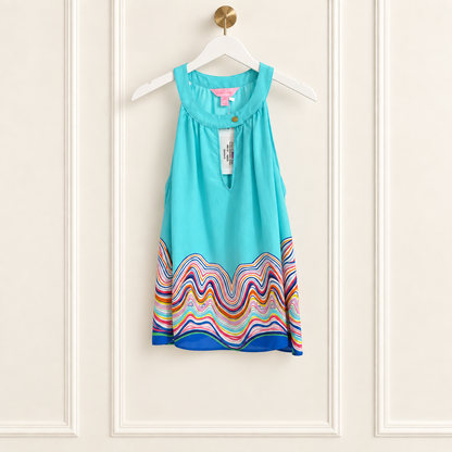 A sleeveless turquoise blue baby dress with a colorful wavy stripe pattern at the hem, hanging on a white hanger against a cream paneled wall.