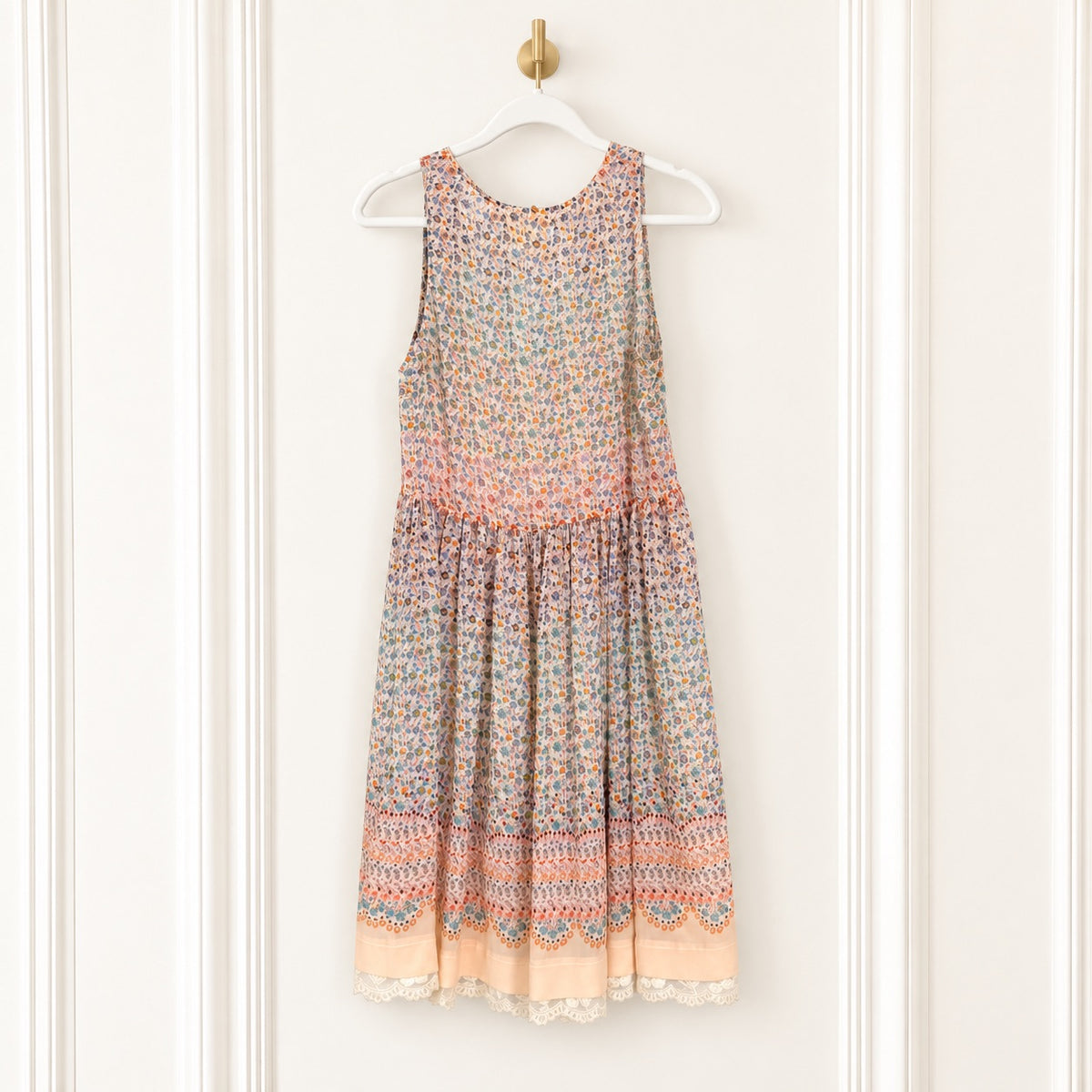 A sleeveless tiered dress with a multicolor floral and geometric pattern, hanging on a white hanger against a white paneled door.