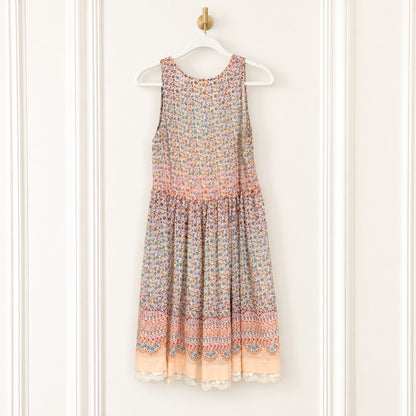 A sleeveless tiered dress with a multicolor floral and geometric pattern, hanging on a white hanger against a white paneled door.