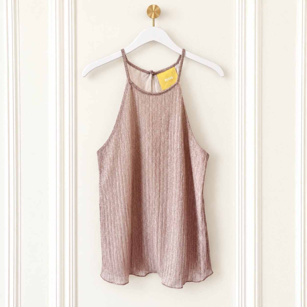 A sleeveless textured camisole top in a dusty rose or mauve color, hanging on a white hanger with a gold hook against a cream paneled wall. A yellow tag is visible at the neckline.
