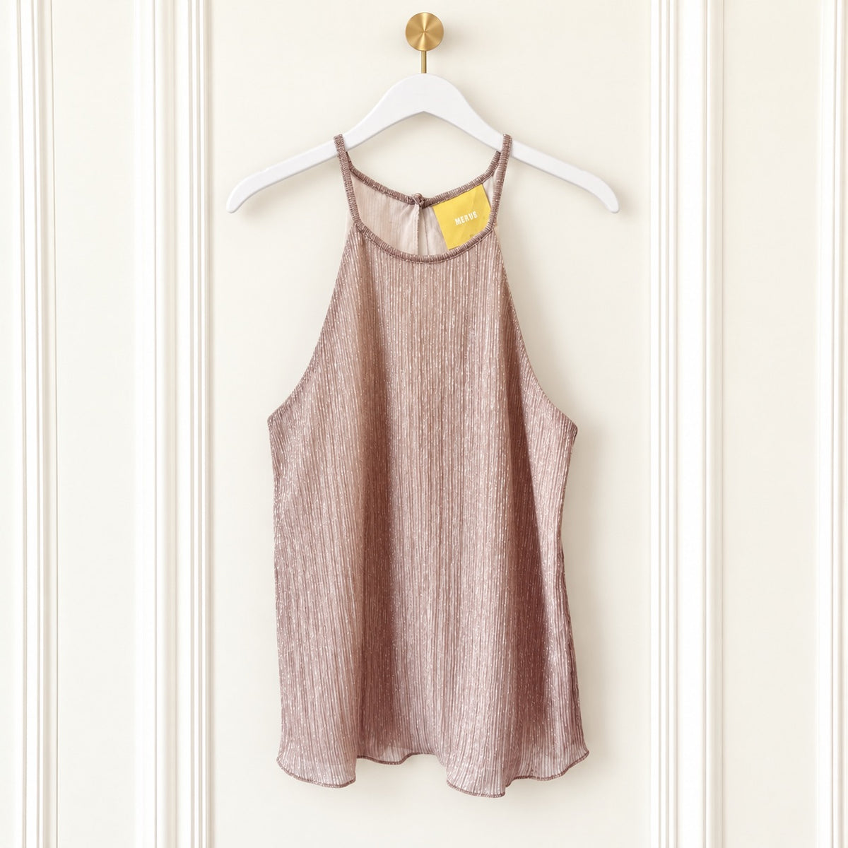 A sleeveless textured camisole top in a dusty rose or mauve color, hanging on a white hanger with a gold hook against a cream paneled wall. A yellow tag is visible at the neckline.