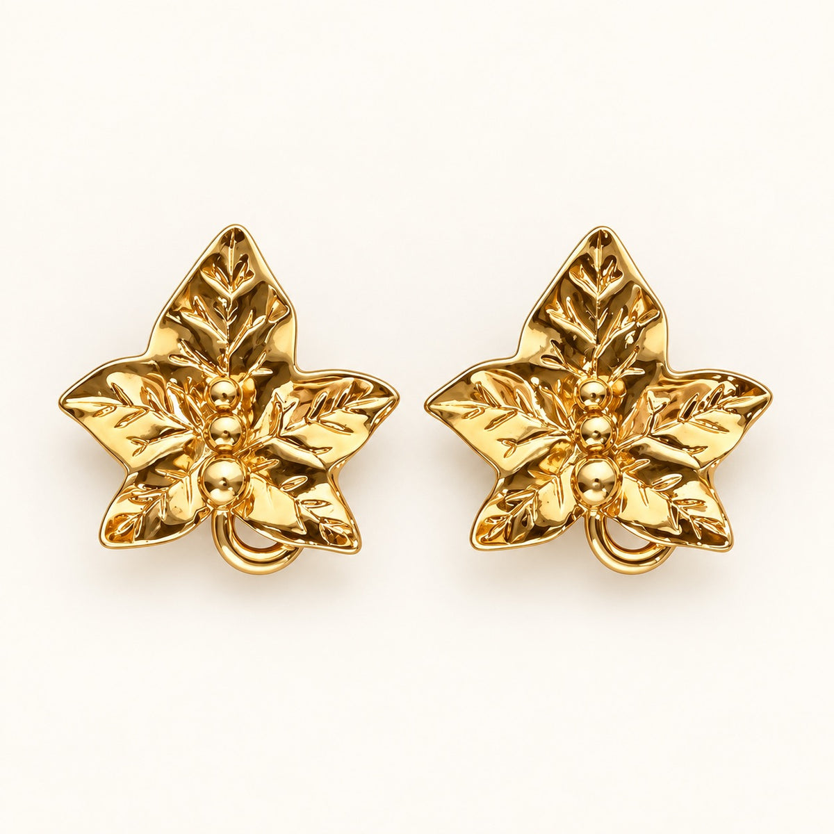 A pair of gold-toned leaf-shaped earrings with a textured, metallic finish, displayed on a clean off-white background.
