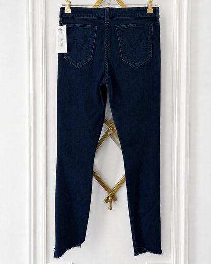 Back view of dark blue denim jeans hanging on a gold hanger against a white paneled wall, showing the back pockets and raw hem.