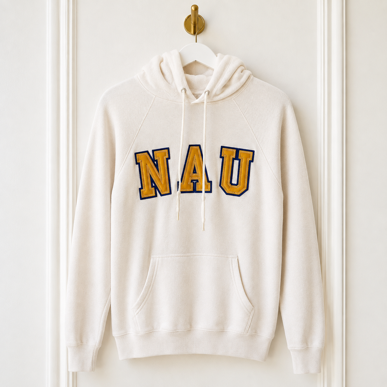An off-white hooded sweatshirt hanging on a white hanger from a gold wall hook, featuring the letters 'NAU' in gold with a navy blue outline across the chest.