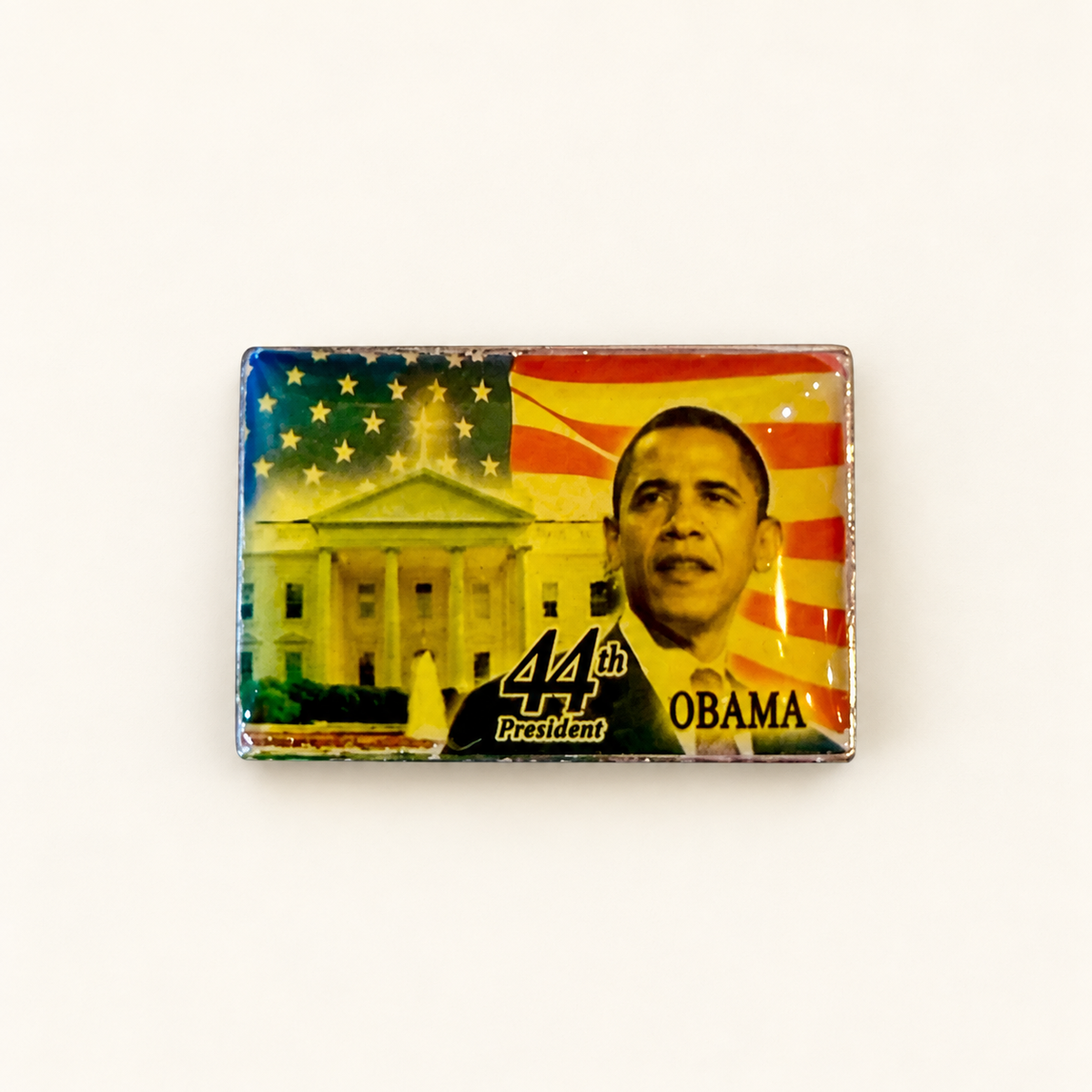 A rectangular commemorative pin or magnet featuring a portrait of Barack Obama, the White House, and an American flag with the text '44th President OBAMA', photographed on a plain white background.
