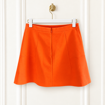 Bright orange A-line mini skirt with a zip closure and side pockets, hanging on a white hanger against a white paneled door.