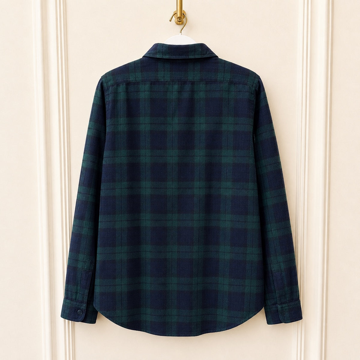 A long-sleeve plaid button-up shirt in dark navy and green, hanging on a white hanger against a cream-colored paneled door.