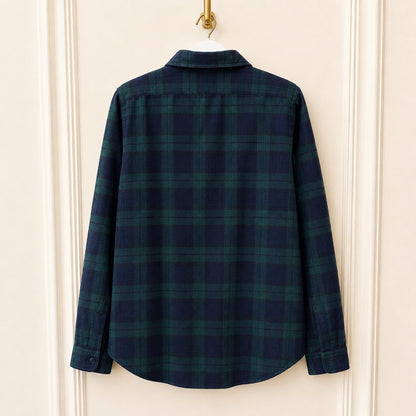 A long-sleeve plaid button-up shirt in dark navy and green, hanging on a white hanger against a cream-colored paneled door.