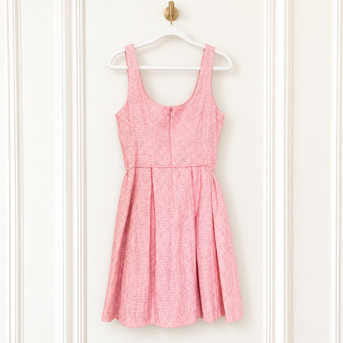 A pink and white textured tweed sleeveless dress hanging on a white plastic hanger against a white paneled door.