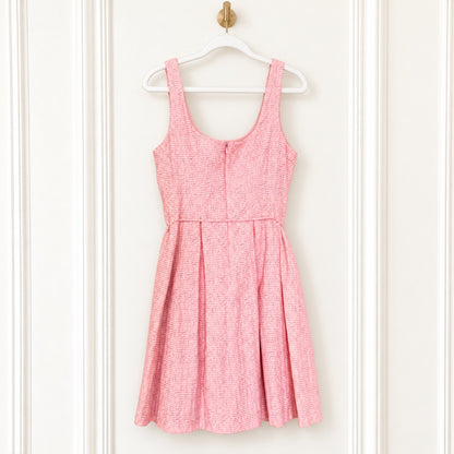 A pink and white textured tweed sleeveless dress hanging on a white plastic hanger against a white paneled door.