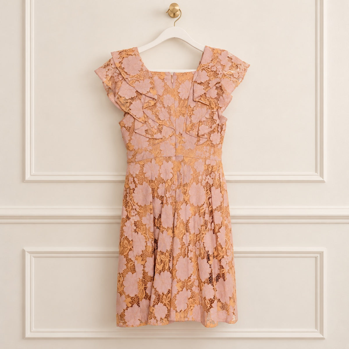 A peach and pink floral lace dress with ruffled cap sleeves, hanging on a white hanger against a cream paneled wall.